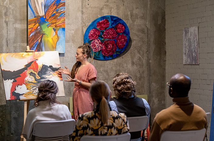 una mujer muestra y habla de una pintura en una galería